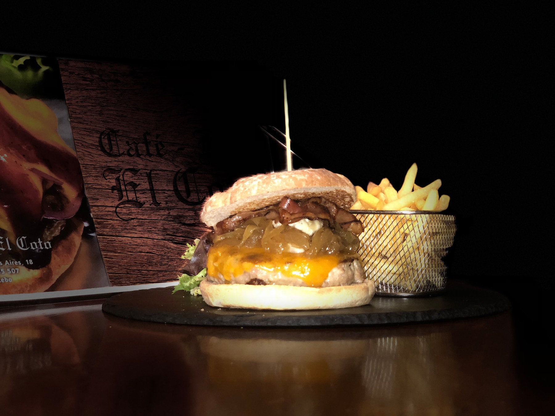 Hamburguesa con cheddar, cebolla caramelizada y bacon junto a la carta de Café El Coto